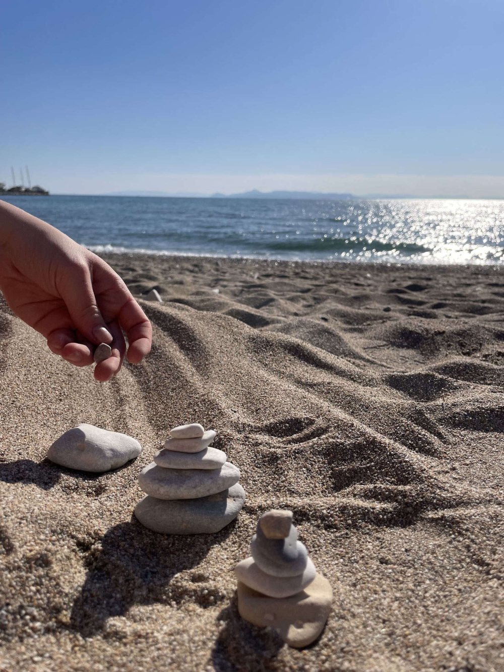 Dłoń układająca kamyk na małym kopczyku nad morzem
